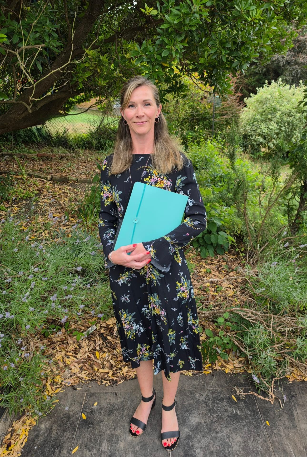 Kirsty Brice in a garden holding her turquoise ceremony folder